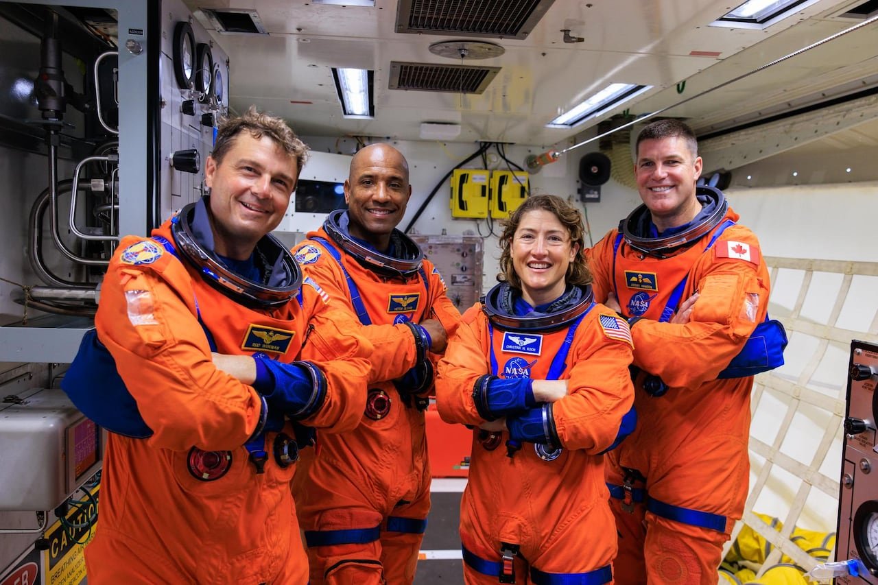 Four astronauts in orange flight gear cross their arms and smile at the camera.
