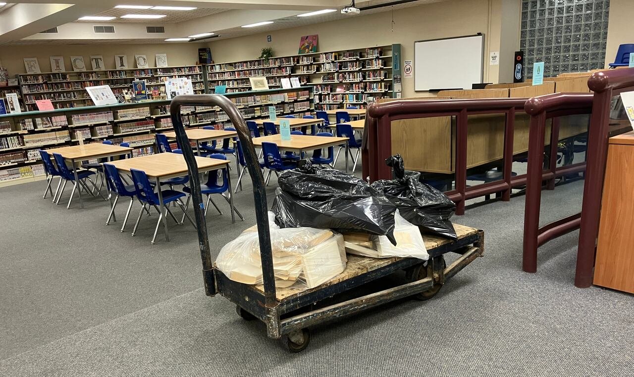 A cart with plastic bags on top of it that appear to be filled with books within a library